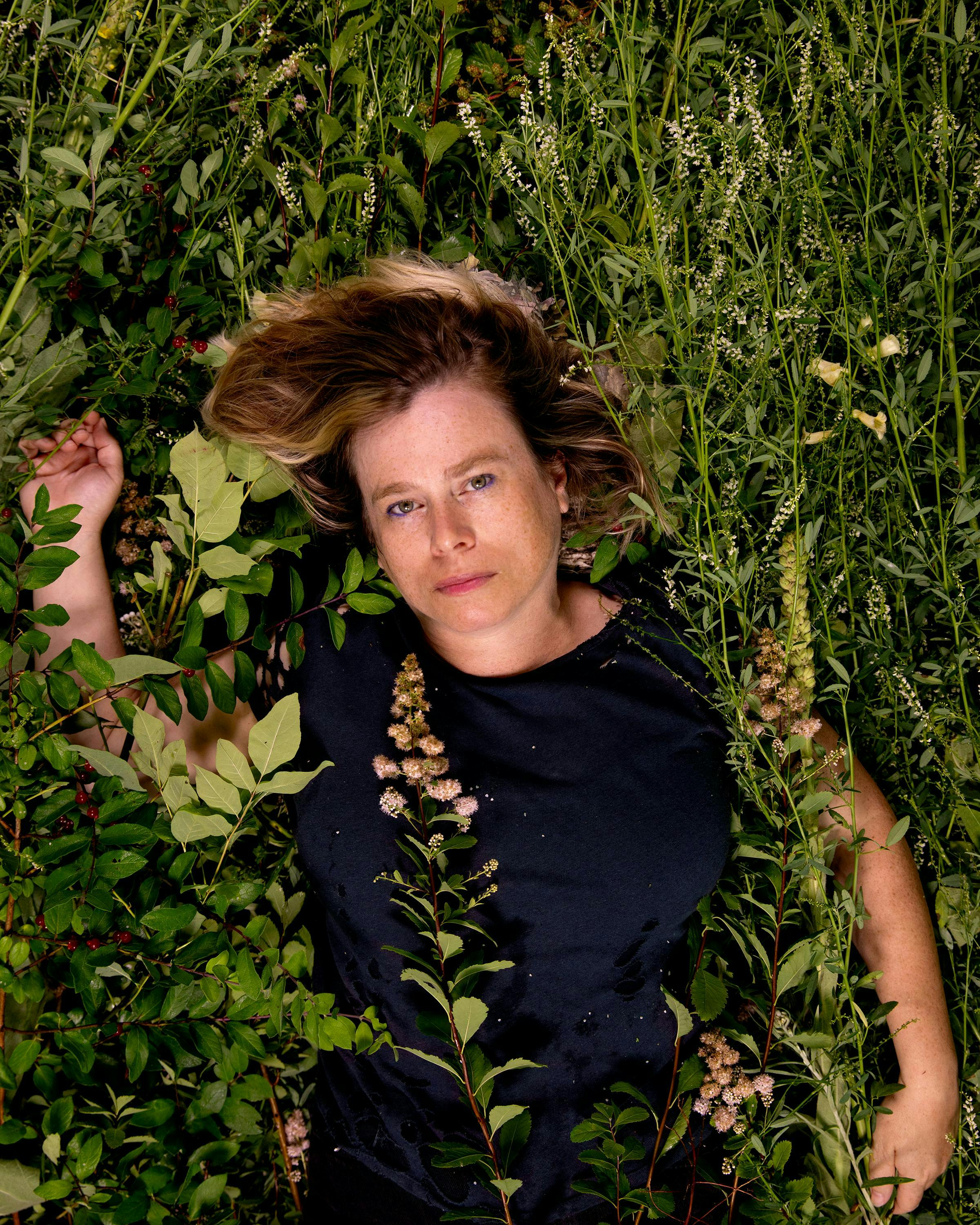 Photo of the artist Lilly McElroy surrounded by plants.