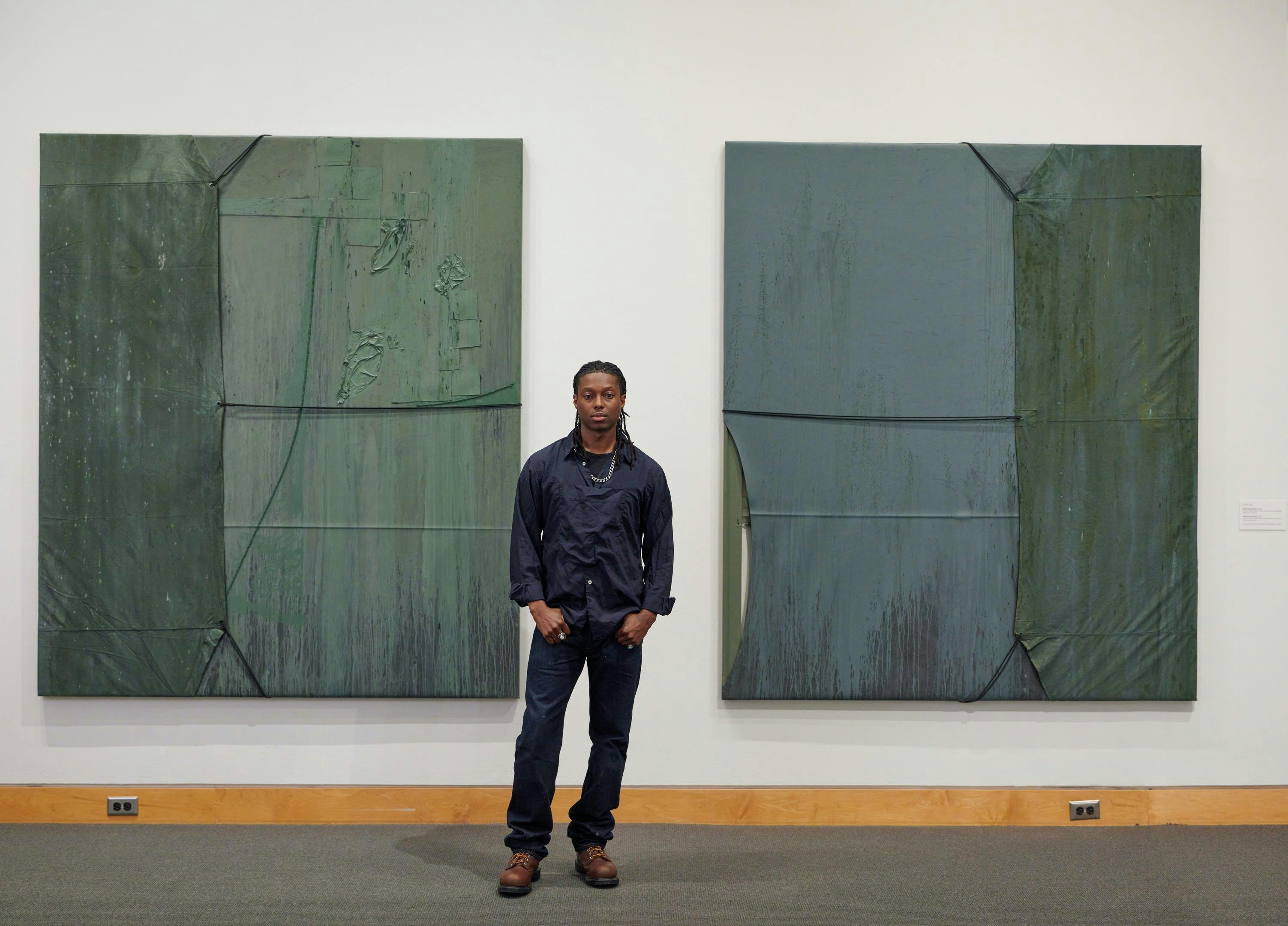 Artist Reginald Sylvester II standing in front of two green minimalist paintings at Kemper Museum.