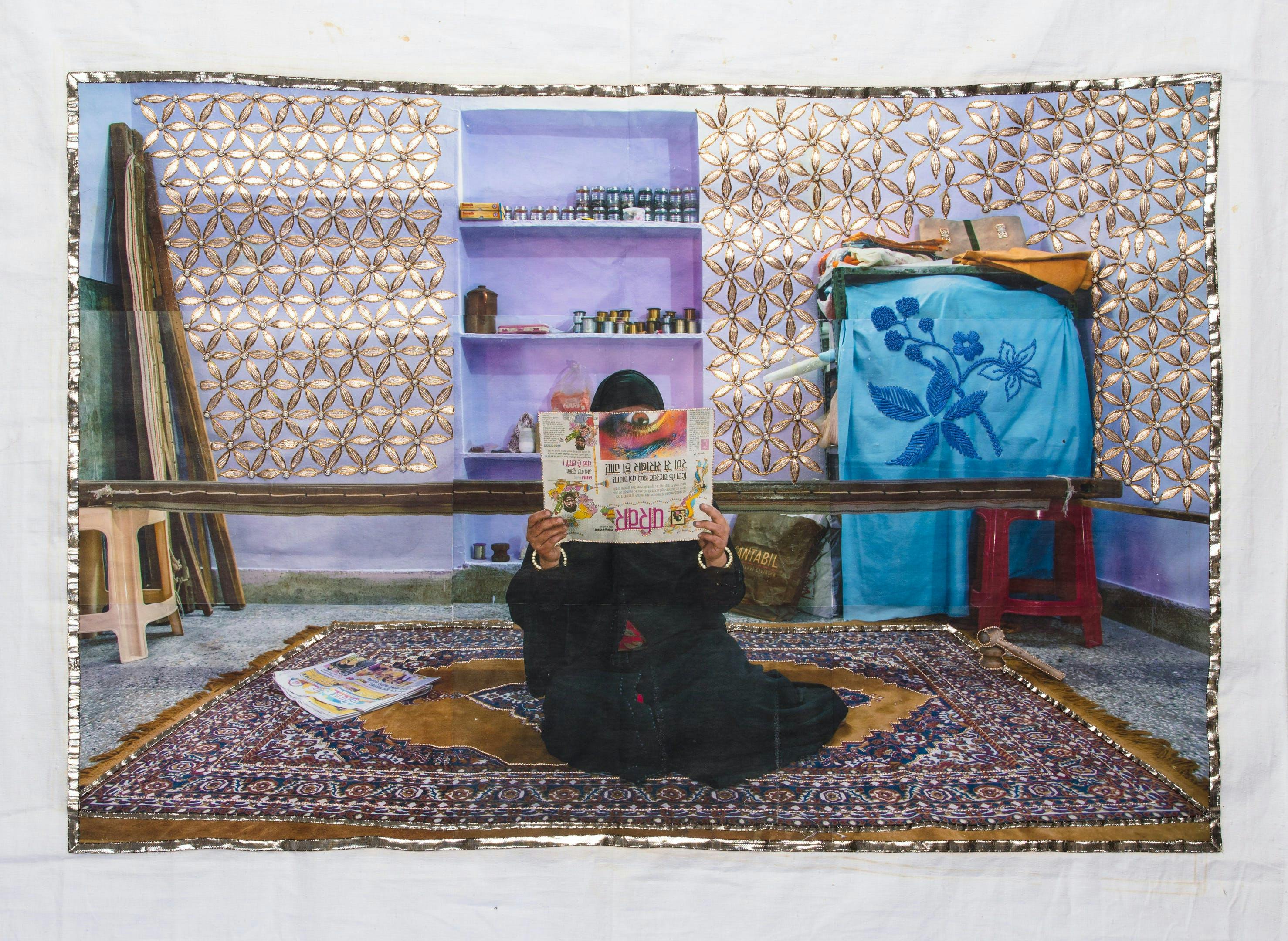 Photograph of woman with a newspaper seated on a rug printed on fabric.